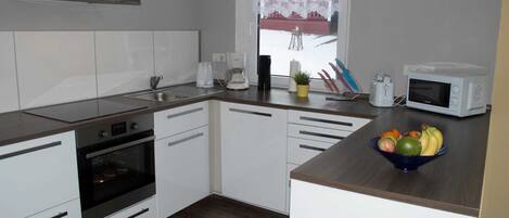 A modern kitchen with white cabinets, a microwave, a coffee maker, and a fruit bowl on the counter.