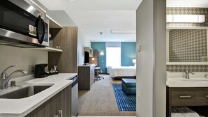 Une chambre d’hôtel moderne équipée d’une kitchenette, d’un lit, d’une salle de bain et d’un espace bureau.