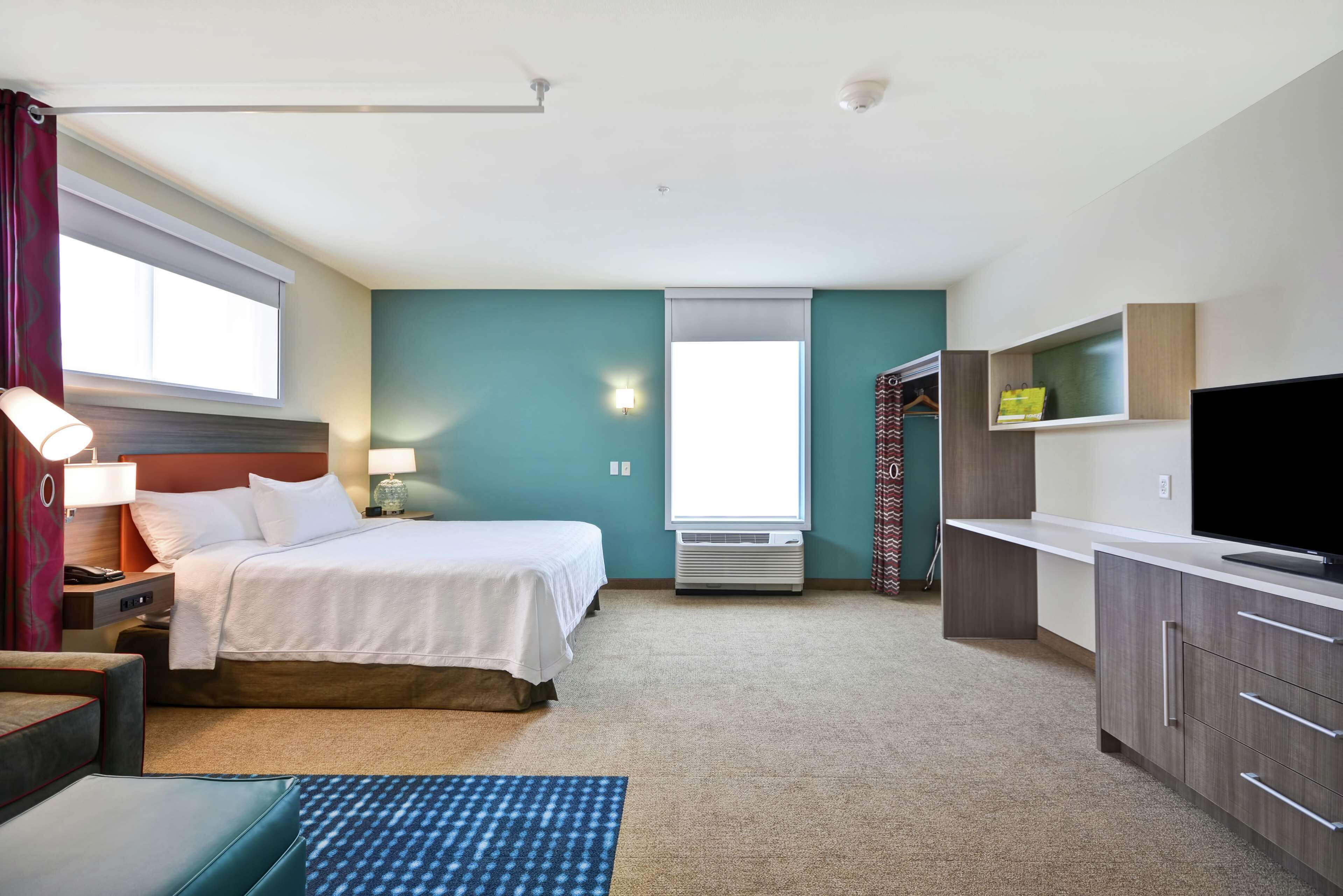 A hotel room with a bed, bedside table, lamp, TV, wardrobe, and a window.