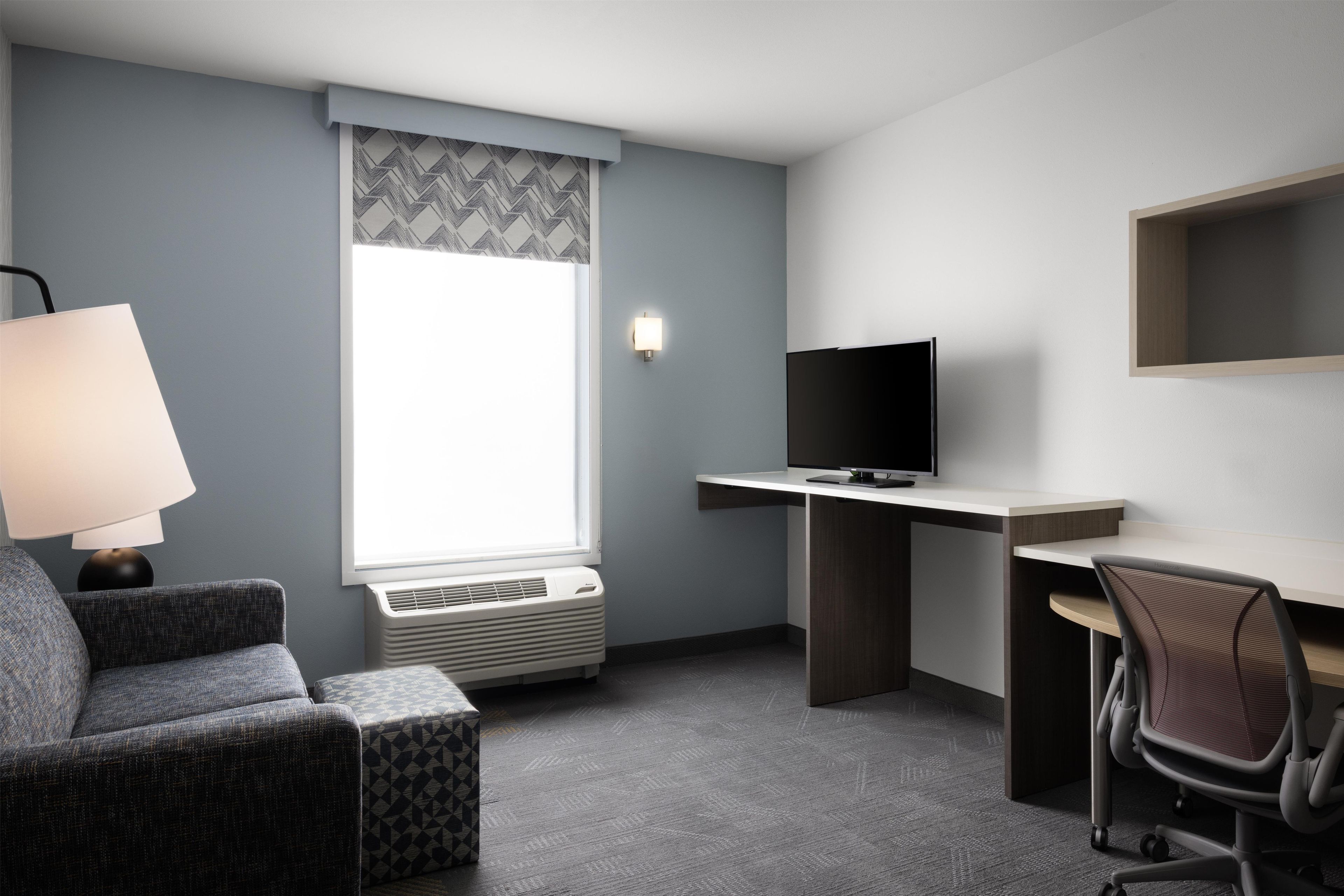 Une chambre d’hôtel équipée d’un bureau, d’une chaise, d’une télévision, d’un climatiseur et d’une lampe.