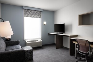 Habitación de hotel con escritorio, silla, televisión, aire acondicionado y lámpara.
