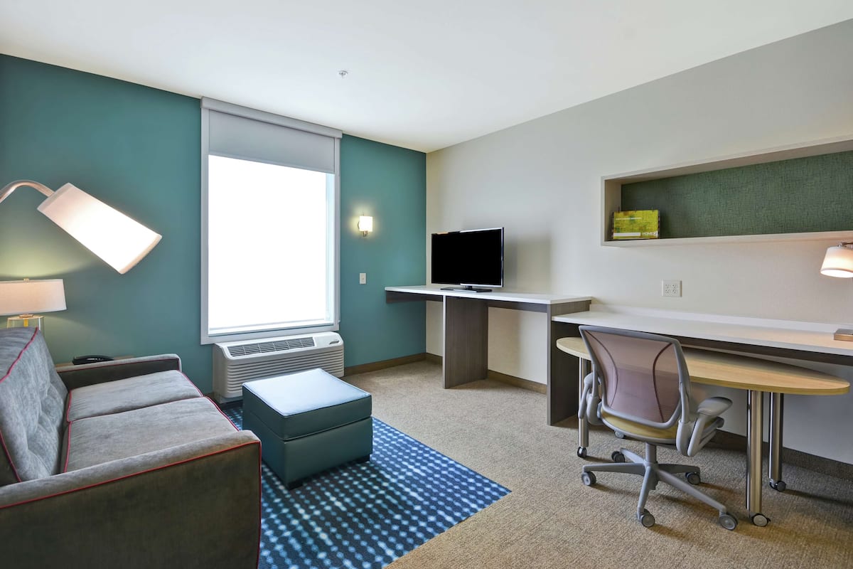 Een kleine hotelkamer met een bank, een bureau, een stoel, een televisie en een raam.