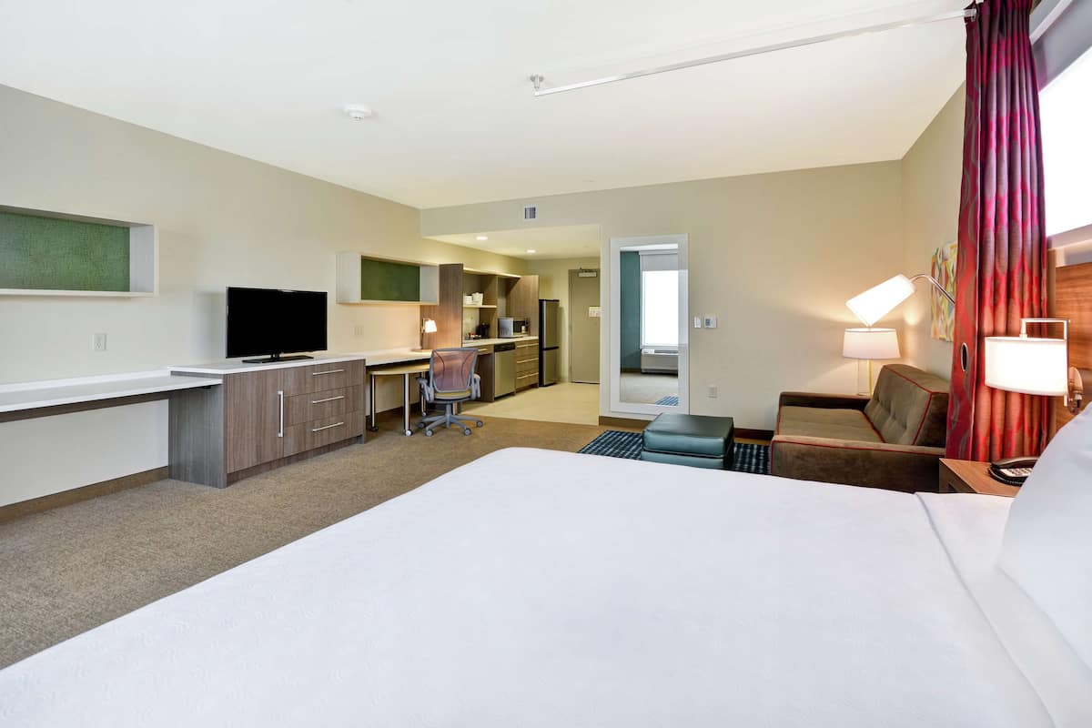 Een hotelkamer met een groot bed, een bureau met stoel, een televisie, een kitchenette en een badkamer.