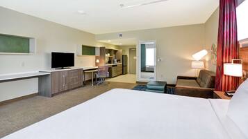 A hotel room with a large bed, a desk with a chair, a television, a kitchenette, and a bathroom.