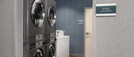 A laundry area with two front-loading washers and a dryer, a storage sign, and a door labeled 'GUEST LAUNDRY'.
