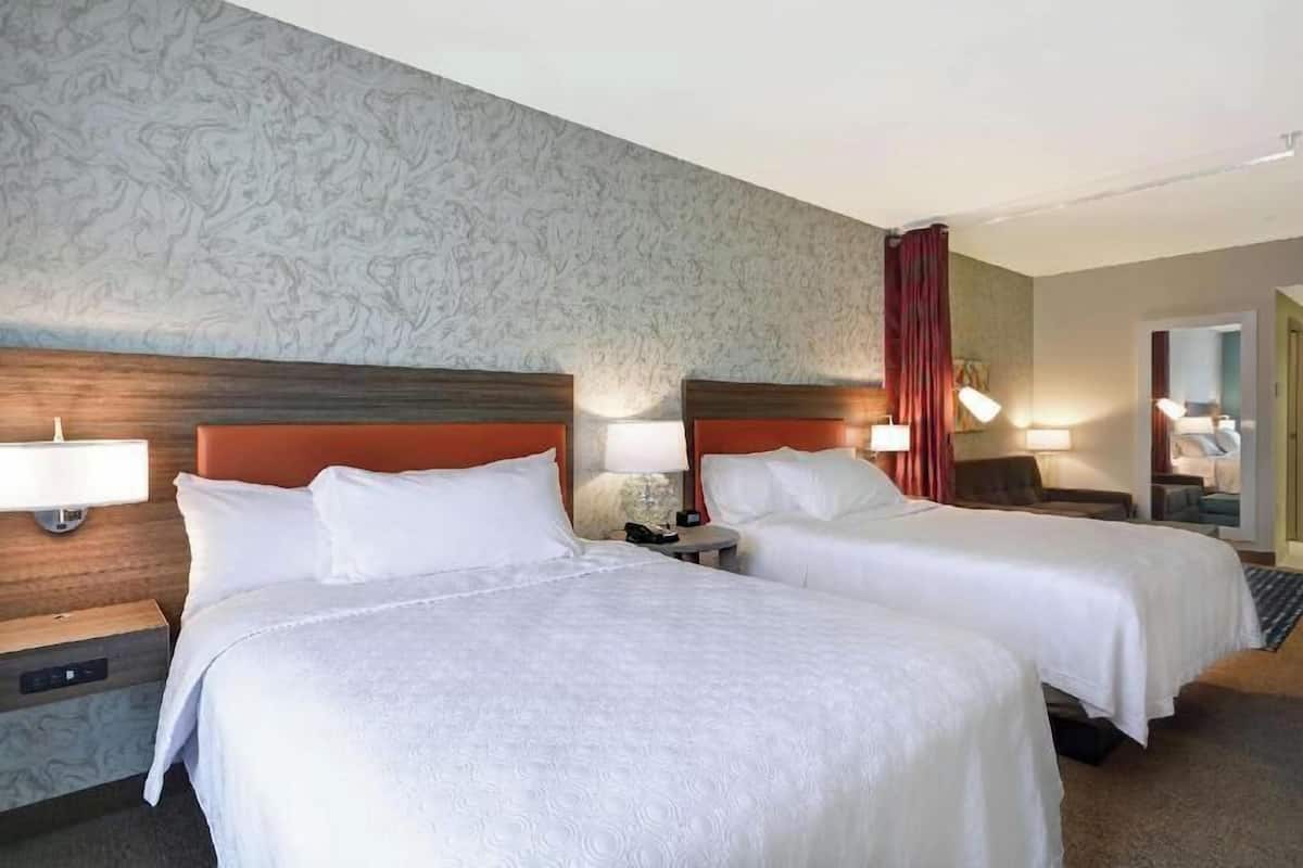 Een hotelkamer met twee bedden, een houten hoofdbord, een behang met patroon en een rood gordijn.
