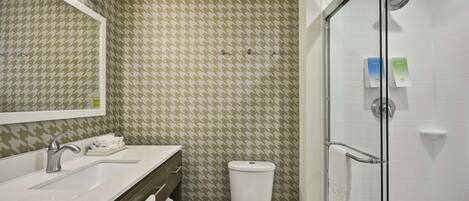 Un baño con pared estampada con diseño pata de perro, un lavabo blanco con grifo plateado, un inodoro y una cabina de ducha de vidrio.