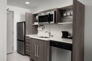 Una cocina moderna con un refrigerador de acero inoxidable, un microondas, una cafetera y un lavavajillas.