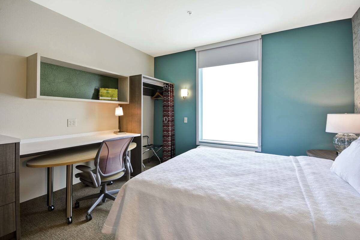 Een hotelkamer met een bed, bureau, stoel en een raam met gordijnen.