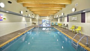 Une piscine intérieure avec des poutres en bois au plafond, une signalisation claire et des chaises jaunes disposées le long du bord de la piscine.