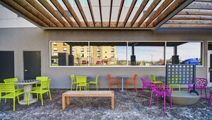 Un espace extérieur aménagé avec des chaises vertes et oranges, un banc en bois et un mur décoré de motifs.