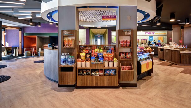 Un kiosque de vente moderne proposant une variété de collations et de boissons, un comptoir de caisse et, en arrière-plan, une enseigne indiquant « Top It Breakfast ».