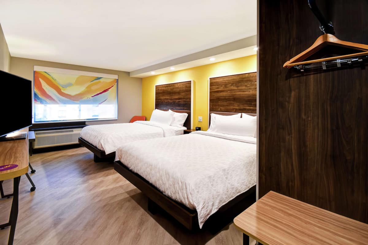 A hotel room with two beds, a desk, a chair, a TV, and a large abstract painting on the wall.