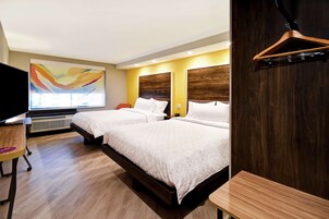 Habitación de hotel con dos camas, un escritorio, una silla, un televisor y un cuadro abstracto grande en la pared.