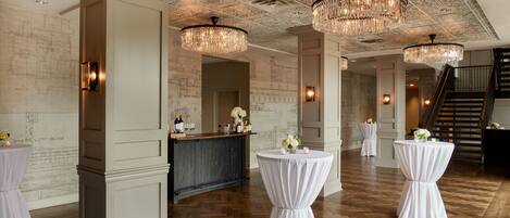 Un vestíbulo amplio con piso de madera en diseño de espiga, una recepción y elegantes candelabros.