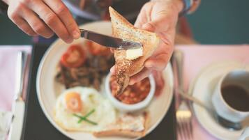 A person spreading butter on toast with a plate of eggs and beans in the background.