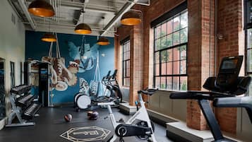 A gym with exercise equipment, a mural, and large windows.