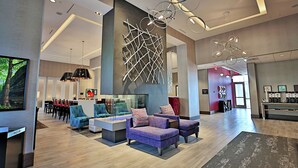 Een ruime lobby met modern meubilair, een groot abstract kunstwerk aan de muur en een plafond met ronde verlichtingsarmaturen.