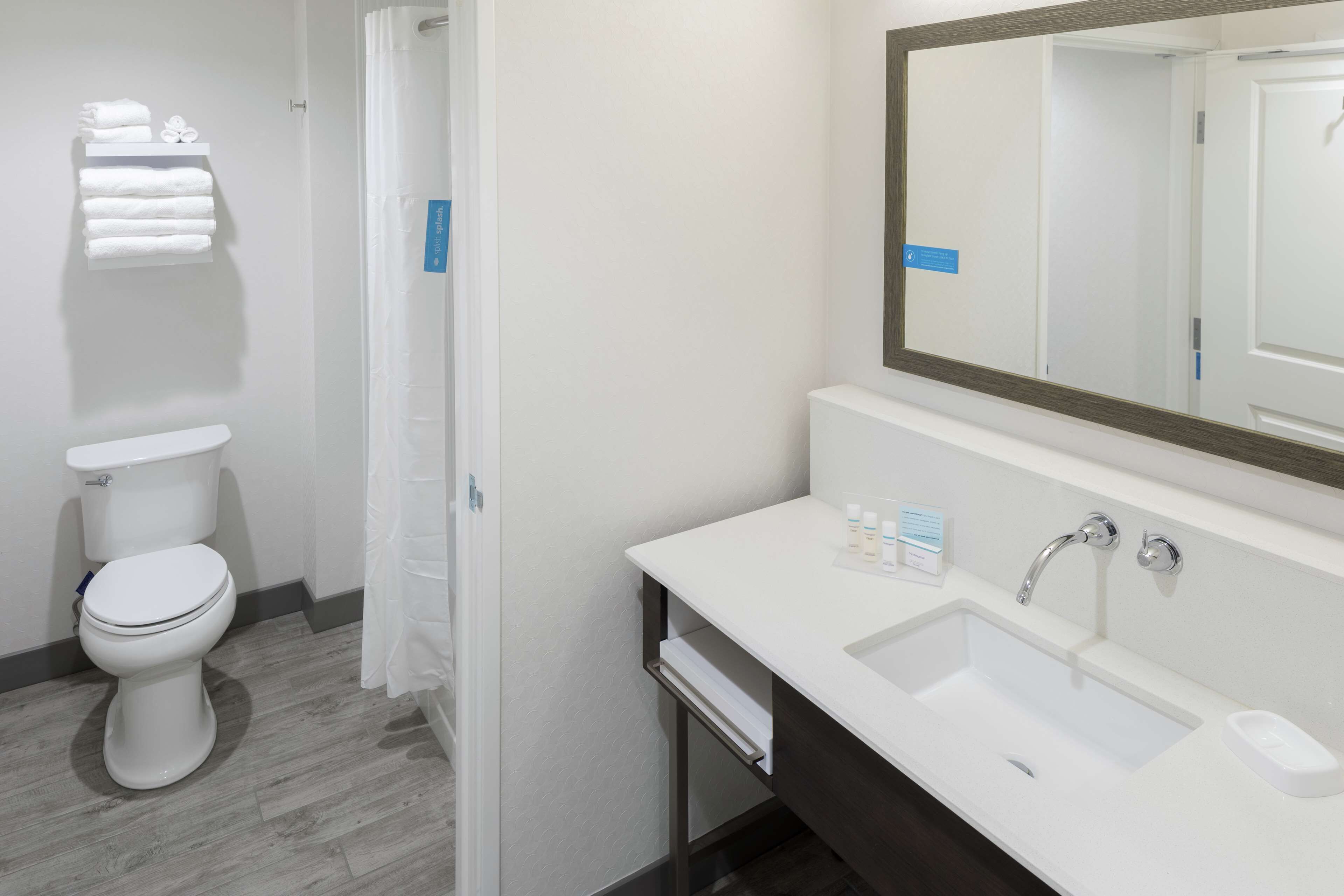 A modern bathroom with a white toilet, a sink with a large mirror, and a towel rack.