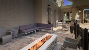 Een terras buiten met een vuurkuil, zitgedeelte en uitzicht op het interieur van het gebouw.