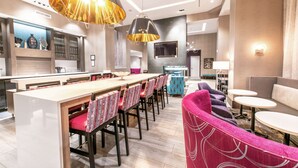Een moderne hotelentree met een lange bar, een zithoek en een aan de muur bevestigde televisie.