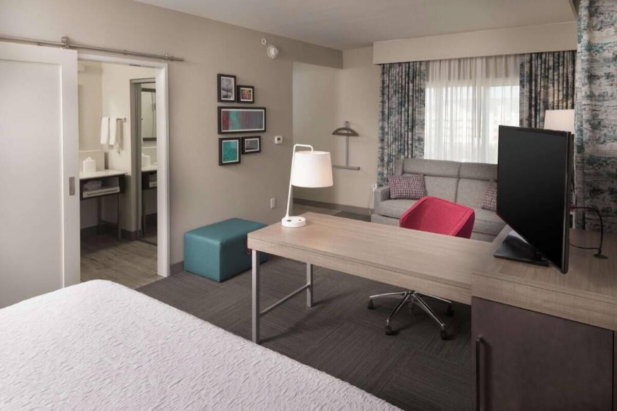 Hotelkamer met een bed, een bureau, een stoel, een televisie, een bank, een lamp en een zichtbare badkamer door een open deur.