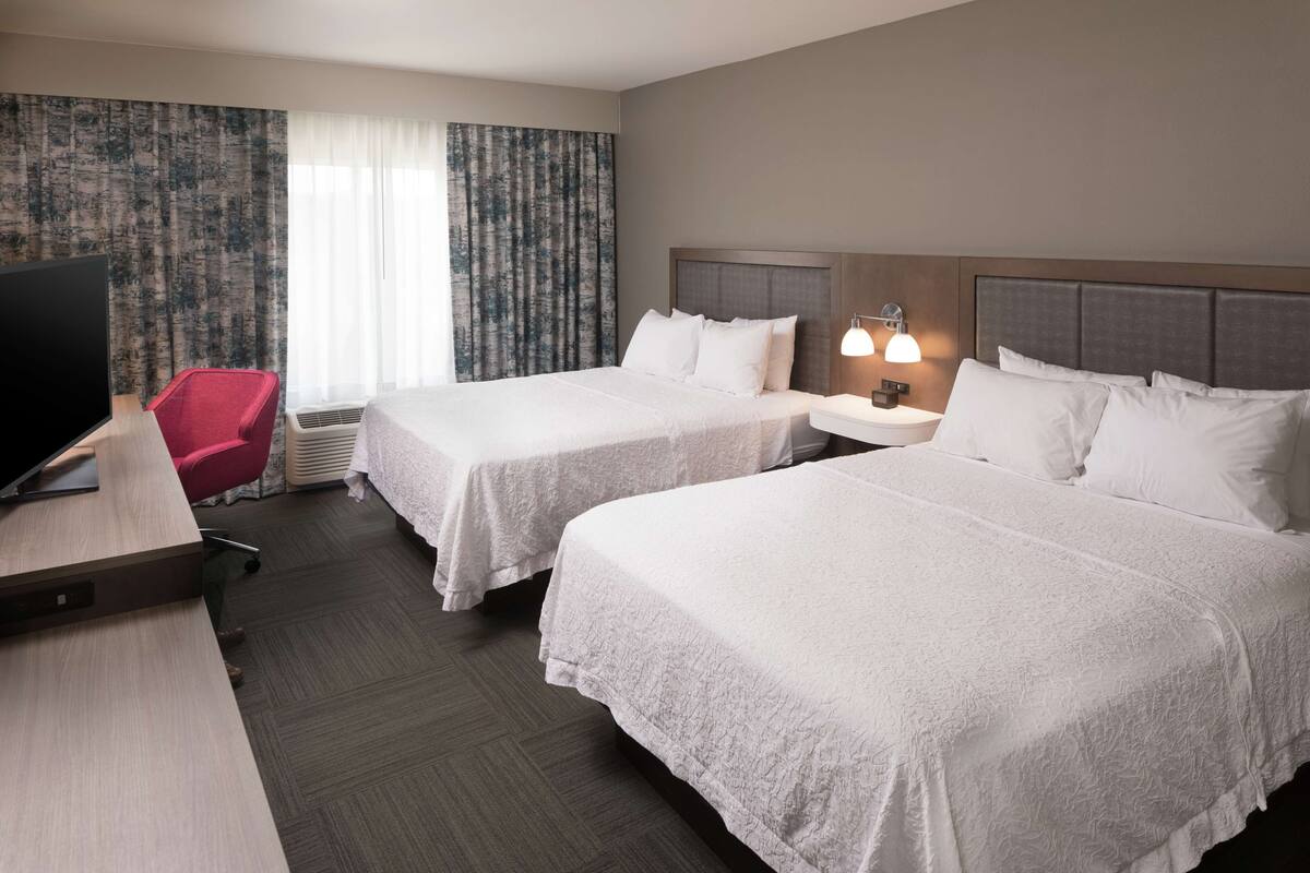 Een hotelkamer met twee bedden, een bureau, een televisie en een rode stoel.