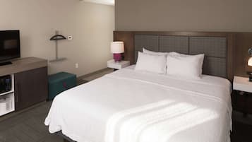 Una habitación de hotel con una cama grande, televisión, escritorio, lámpara y mesita de noche.