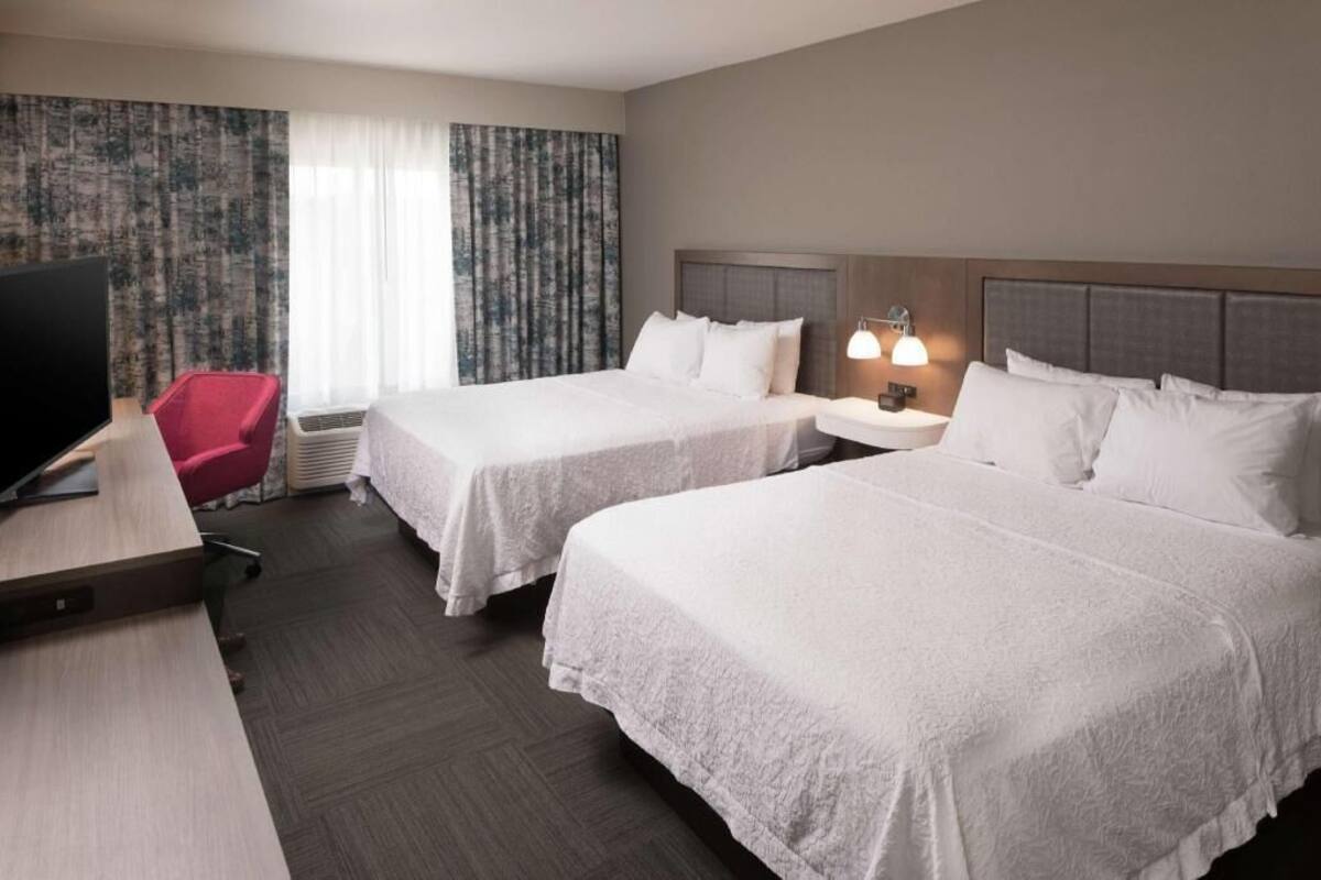 Een hotelkamer met twee bedden, een bureau, een televisie en een rode stoel.