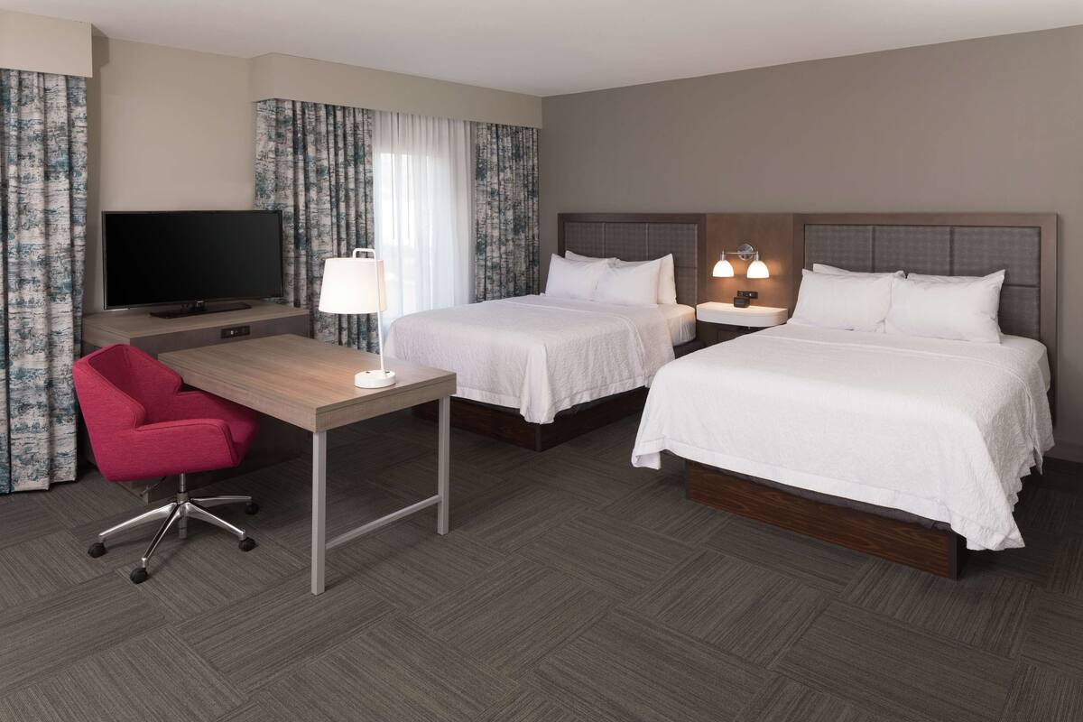Een hotelkamer met twee bedden, een bureau met stoel, een televisie en een lamp.