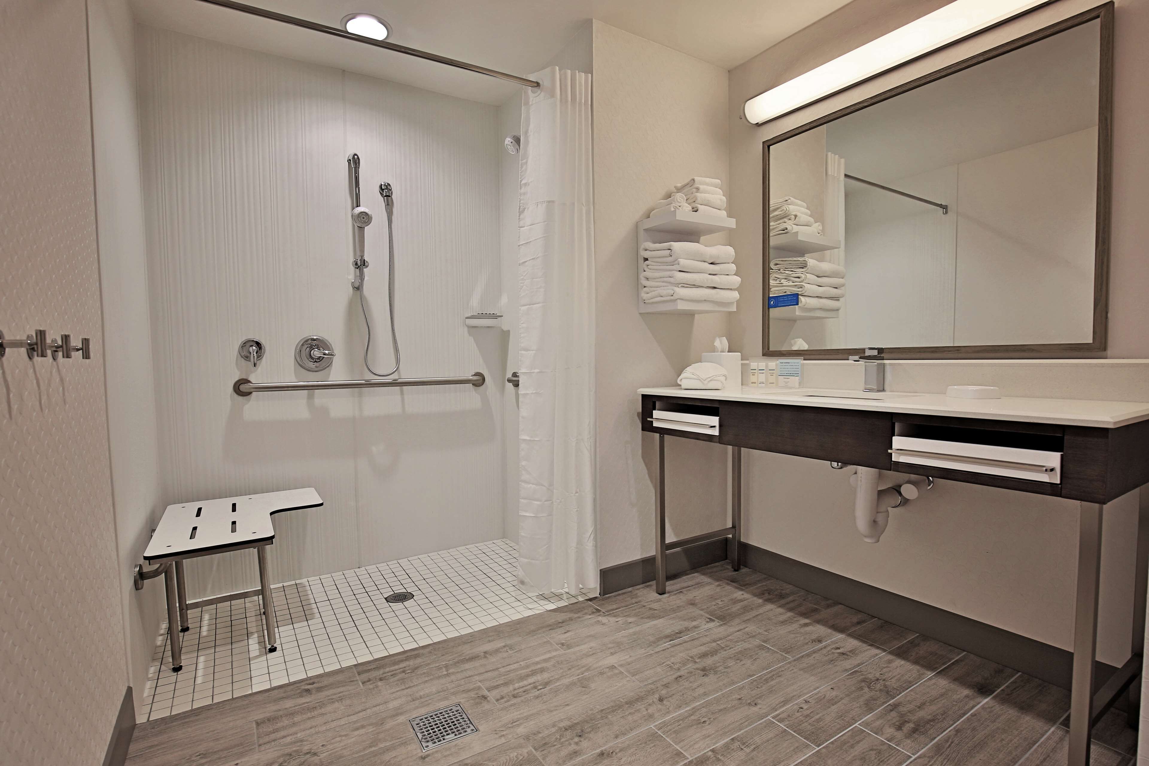Une salle de bain moderne avec une douche à l’italienne, un meuble-lavabo avec un miroir et des serviettes soigneusement pliées.