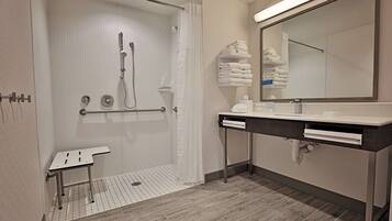 Une salle de bain moderne avec une douche à l’italienne, un meuble-lavabo avec un miroir et des serviettes soigneusement pliées.
