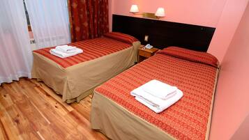 Deux lits simples avec une literie rouge et beige, un plancher en bois et une table de chevet avec un téléphone.