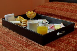 Bandeja de desayuno con croissants, muffins, un vaso de jugo de naranja, una taza de café y un tazón de fruta sobre una colcha estampada.