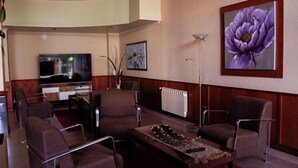 A modern living room with a flat-screen TV, two armchairs, a coffee table, and a floor lamp. - Villa Brescia Hotel (Ushuaia)