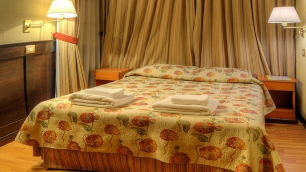A double bed with floral bedding, wooden headboard, and two bedside lamps. - Villa Brescia Hotel (Ushuaia)