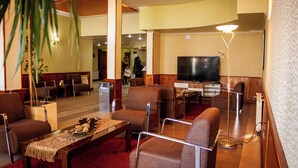 A hotel lobby with a red carpet, brown leather chairs, a wooden coffee table, a large flat-screen TV, and a potted plant. - Villa Brescia Hotel (Ushuaia)