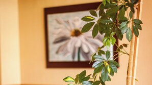 A potted plant in a corner of a room with a red carpet, a framed picture on the wall, and a wooden chair. - Villa Brescia Hotel (Ushuaia)