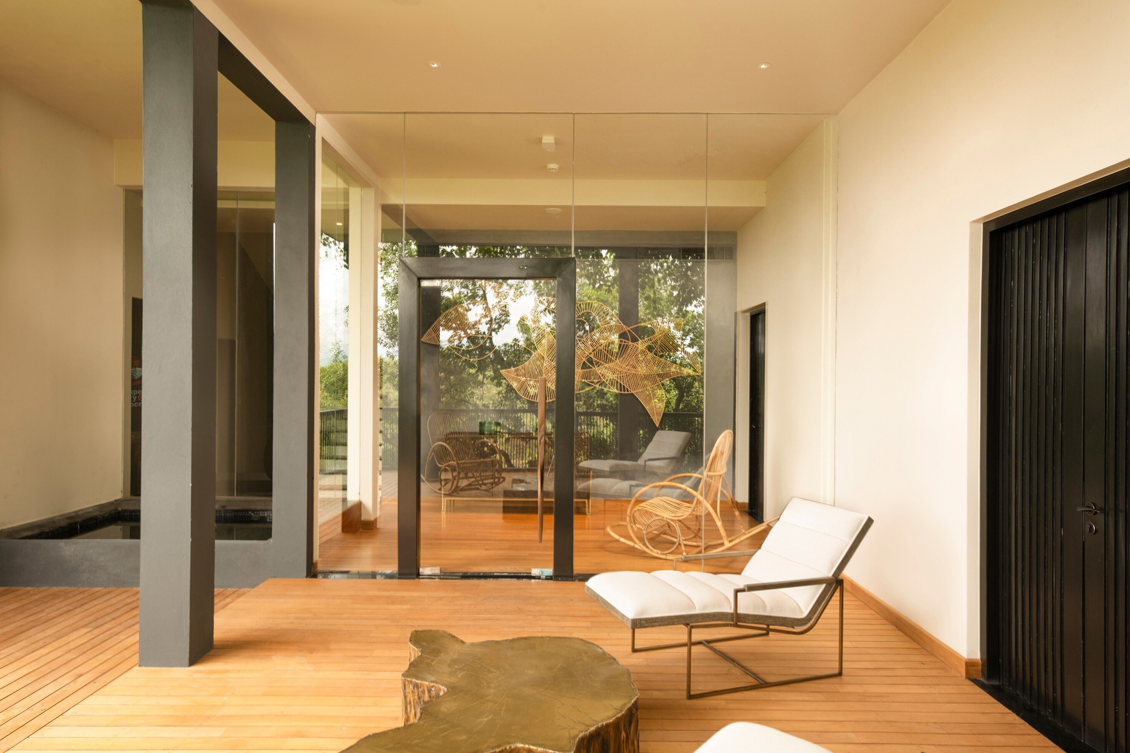 A modern interior with a wooden floor, glass doors leading to a patio with outdoor furniture, and a black door on the right.
