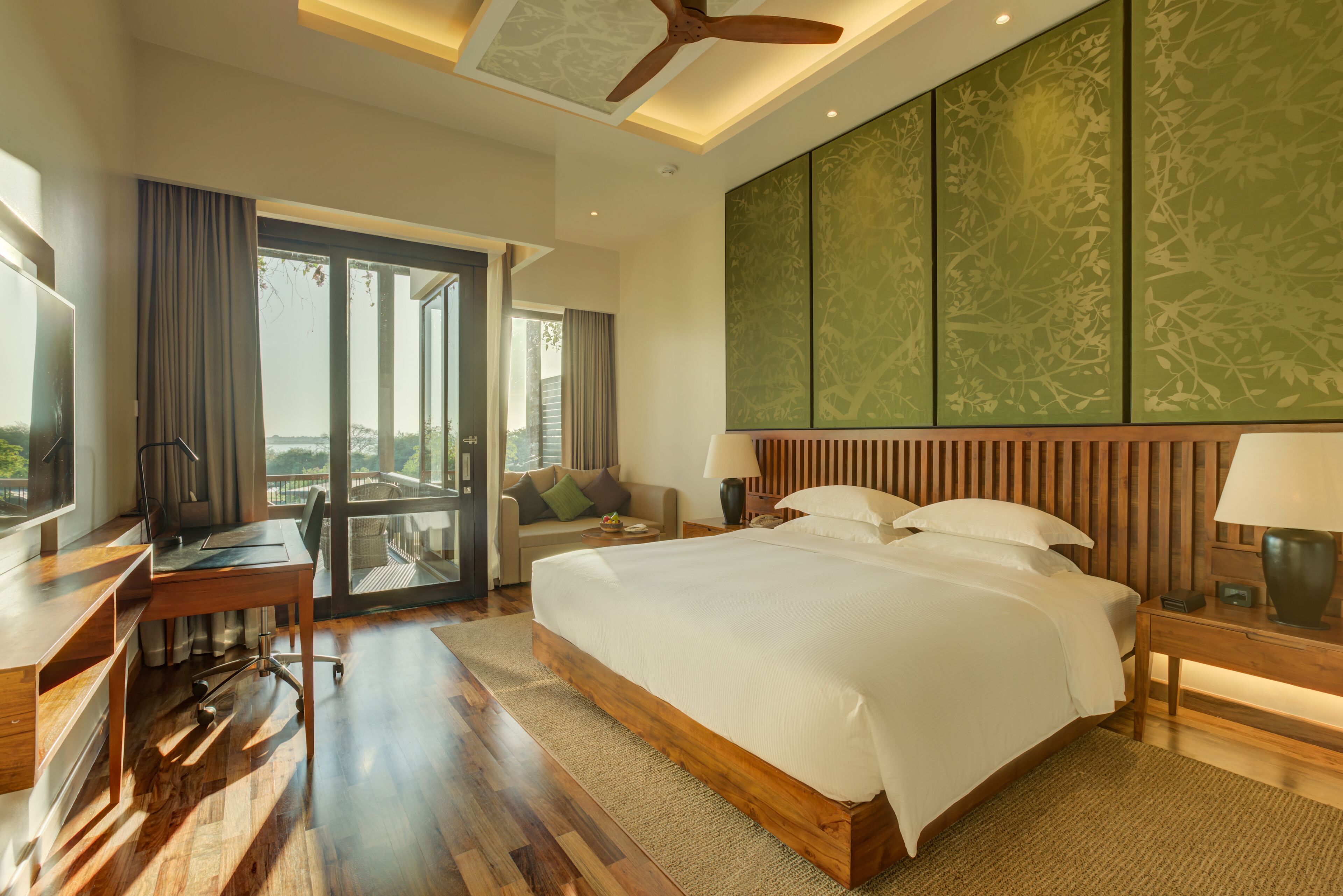 A modern hotel room with a large bed, a desk, a chair, and a balcony with a view.