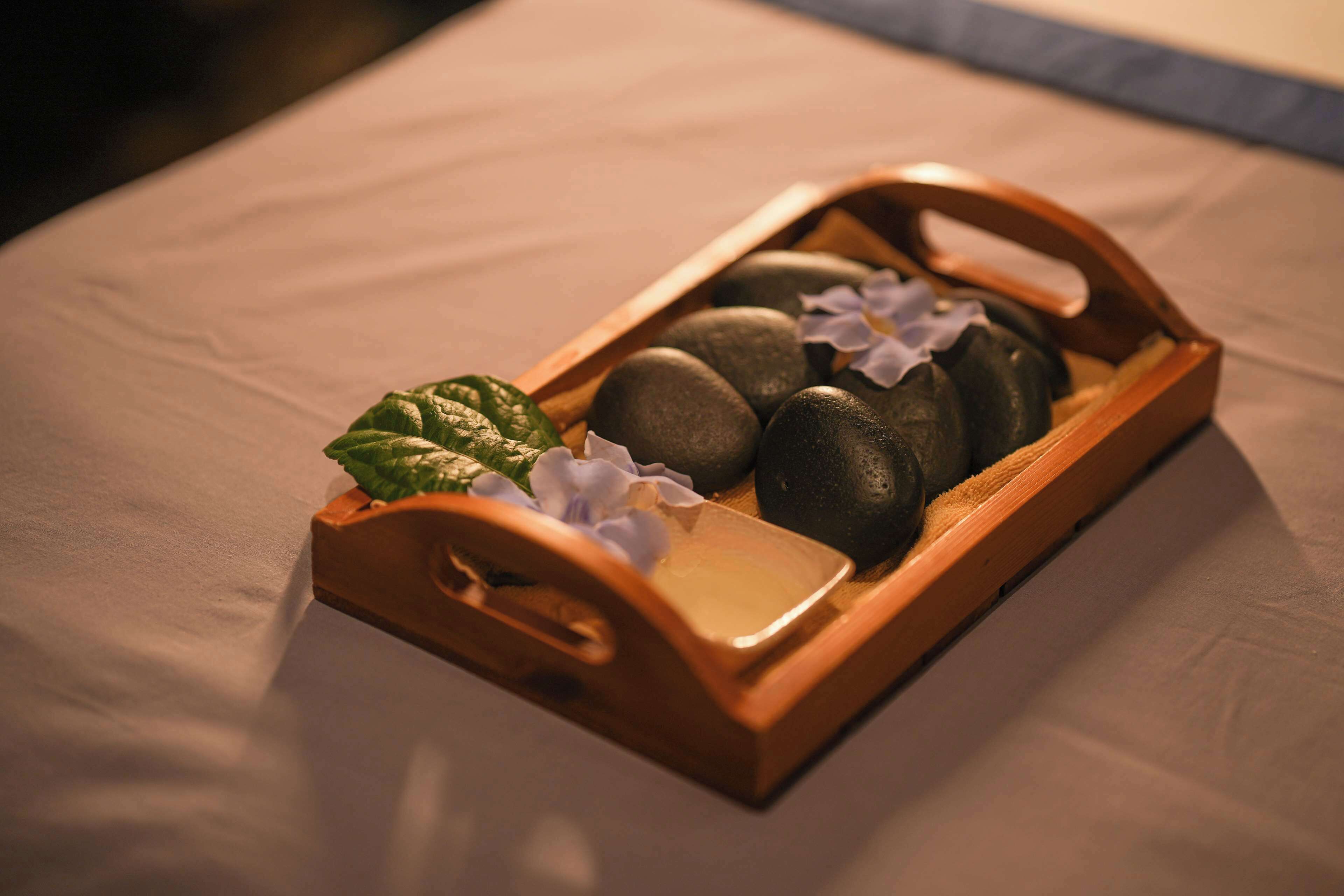 A wooden tray with stones and a green leaf on a bed.