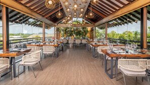 A restaurant with wooden tables and wicker chairs, large windows, and hanging light fixtures. - DoubleTree by Hilton Weerawila Rajawarna Resort (Weerawila)