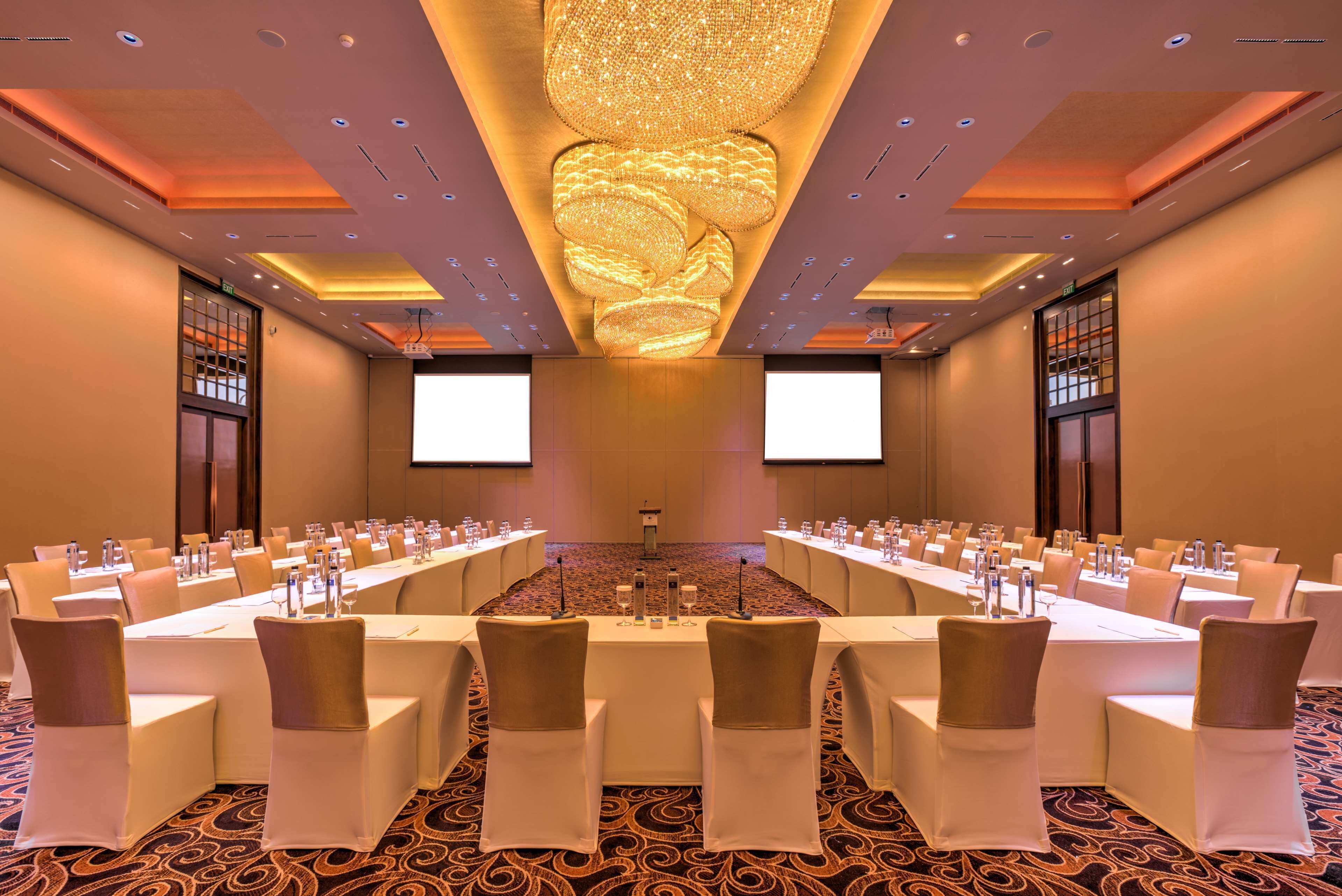 A conference room with a long table, chairs, and a large screen at the front.