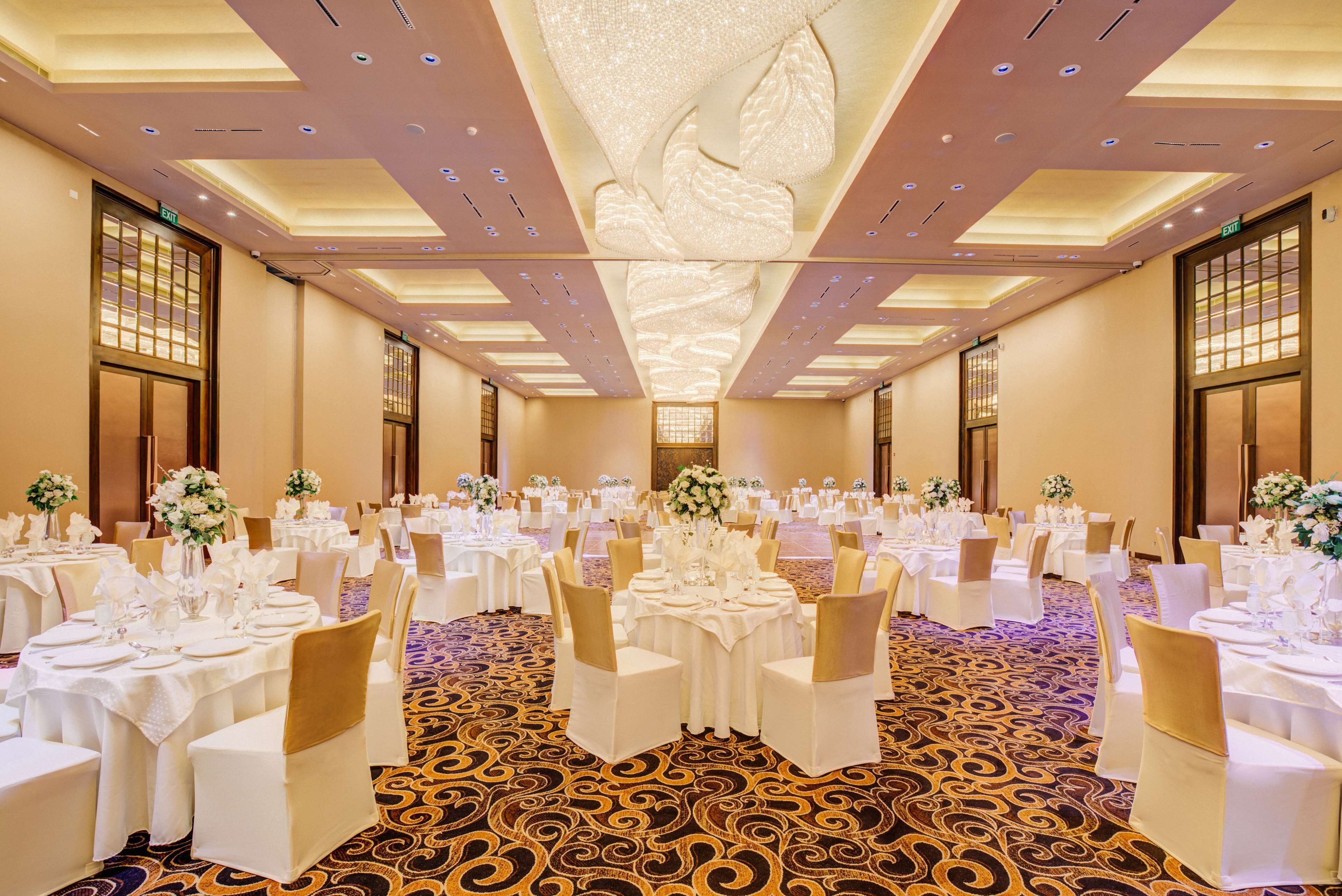 A banquet hall with round tables, white tablecloths, and gold chairs.