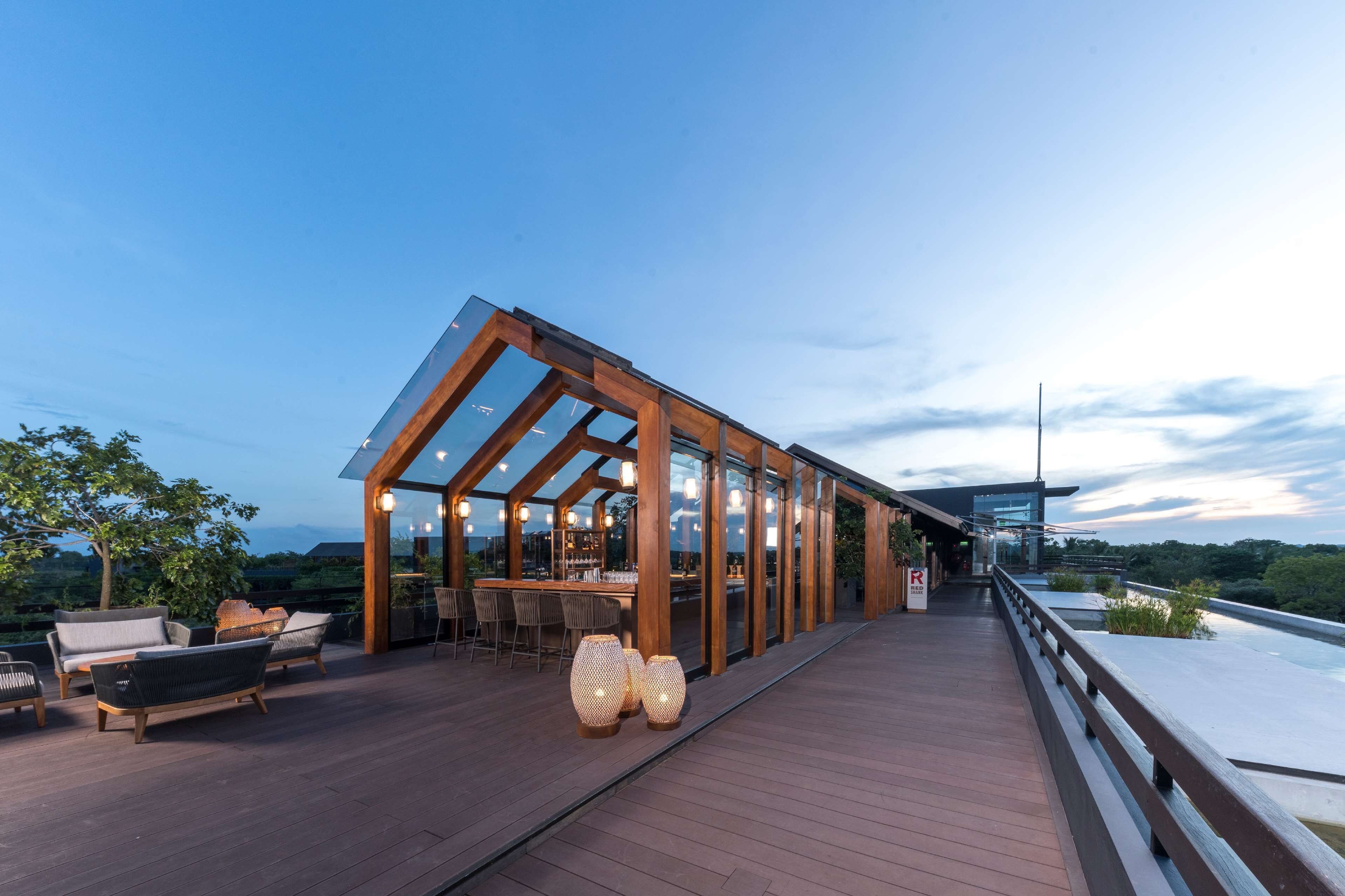 A modern outdoor deck with wooden furniture and glass walls, overlooking a scenic landscape.