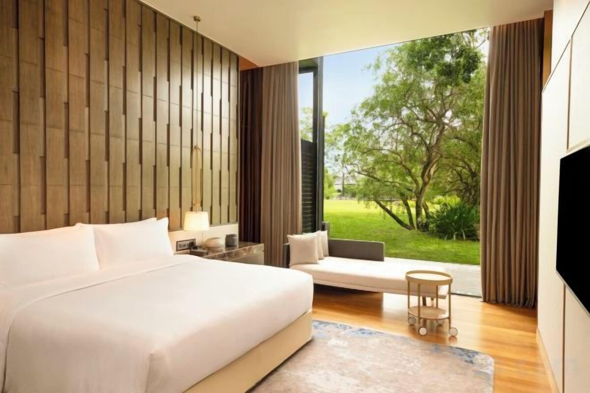 A bedroom with a large bed, a seating area, and a view of a garden.