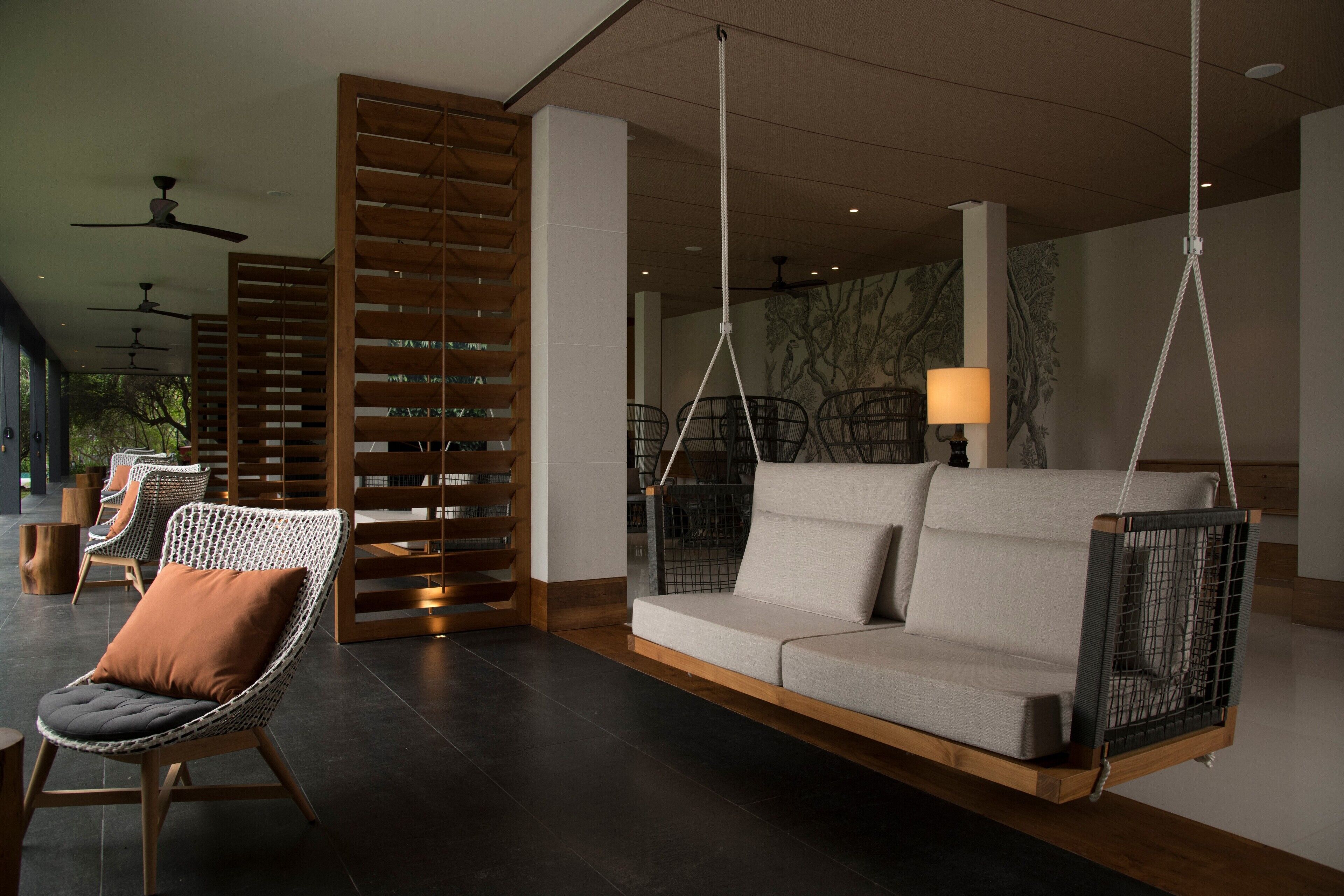 A modern lounge area with a hanging swing, cushioned chairs, and a wooden slatted wall.