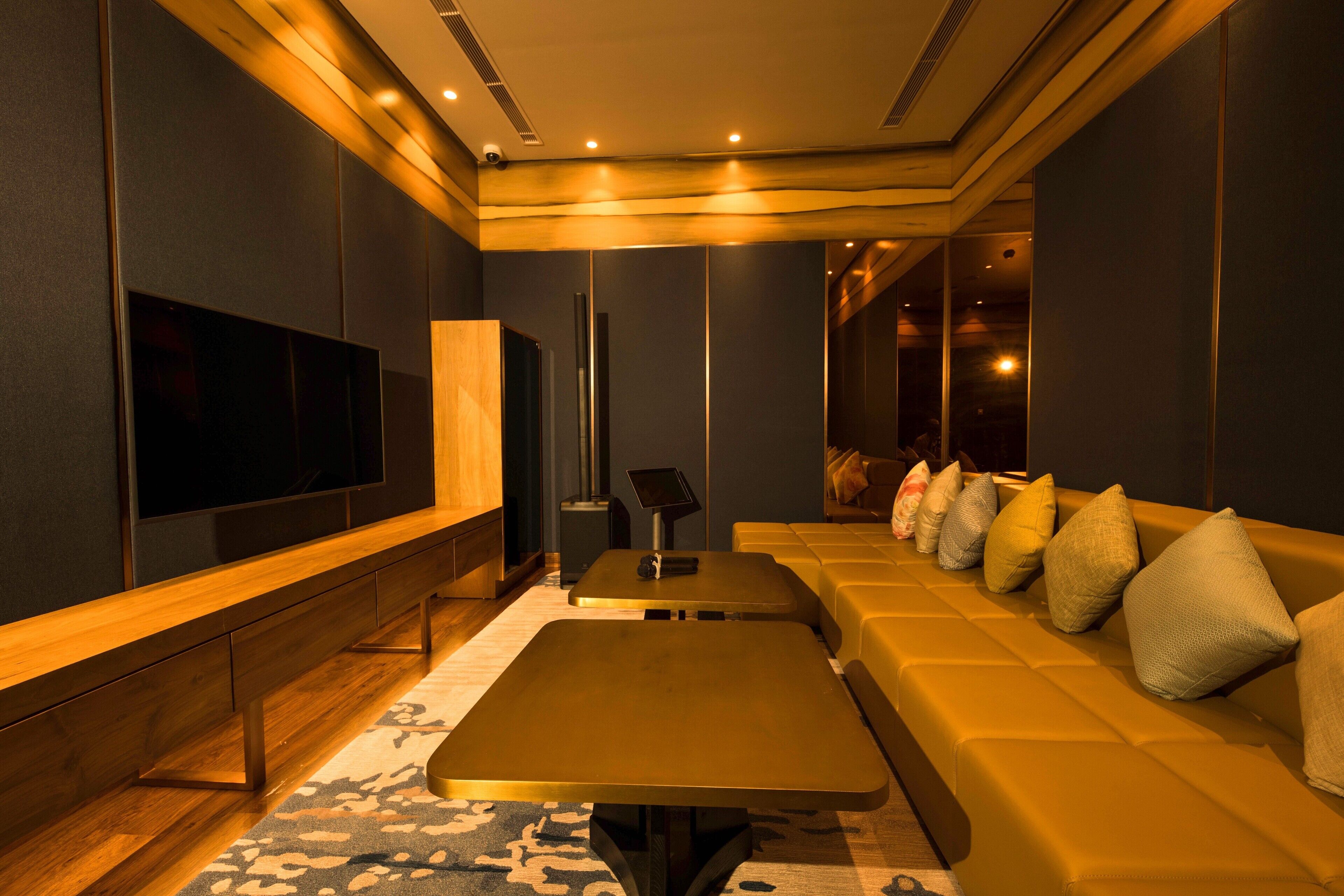 Een moderne woonkamer met een grote flatscreen-tv, een bank met kussens, een salontafel en een kamerkleed met dessin.