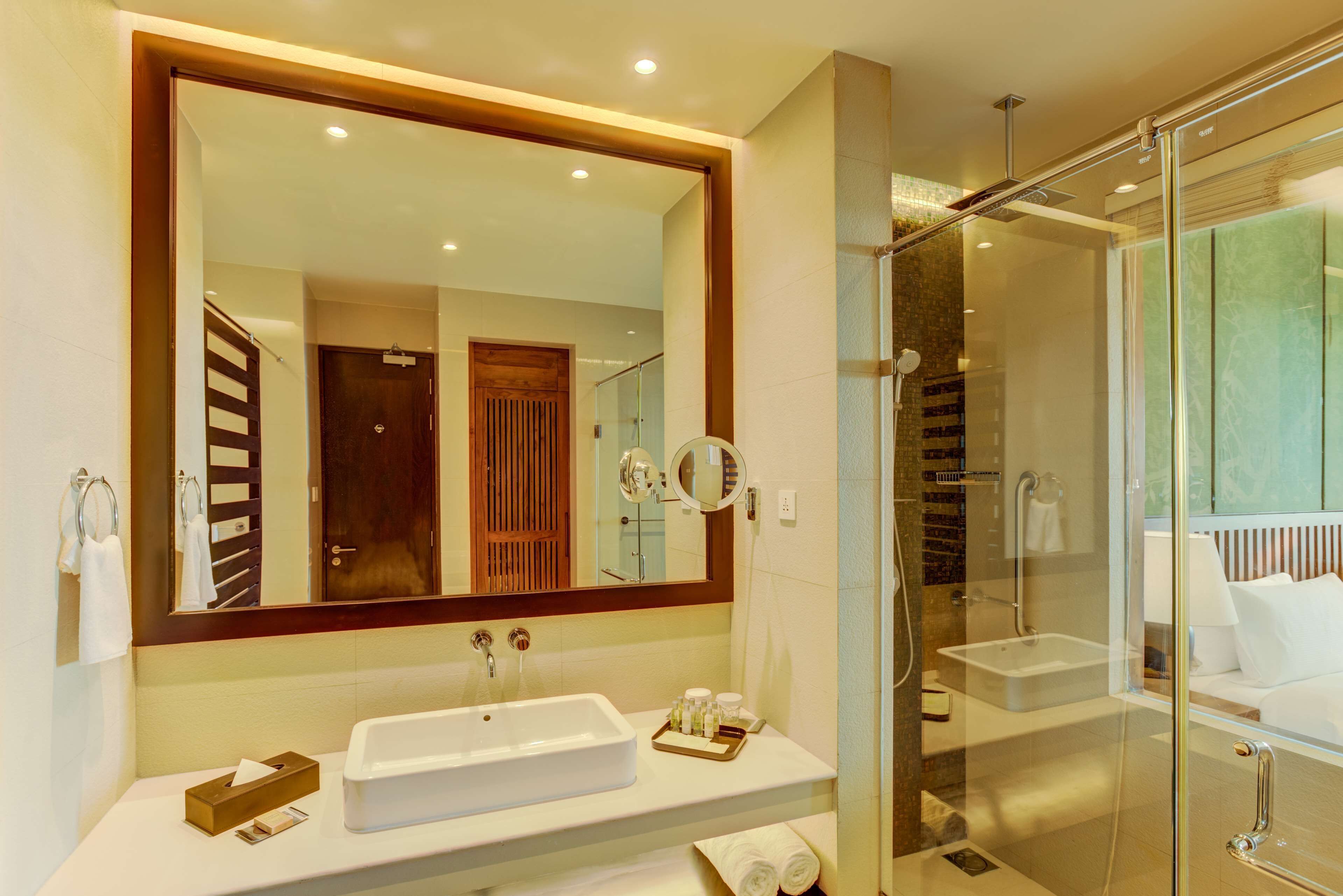 Un baño moderno con un espejo grande, un lavabo, cabina de ducha de vidrio y una puerta de madera.