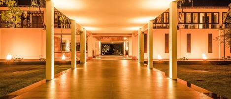 A well-lit, spacious corridor with a modern architectural design, featuring a central pathway flanked by columns and a symmetrical layout.